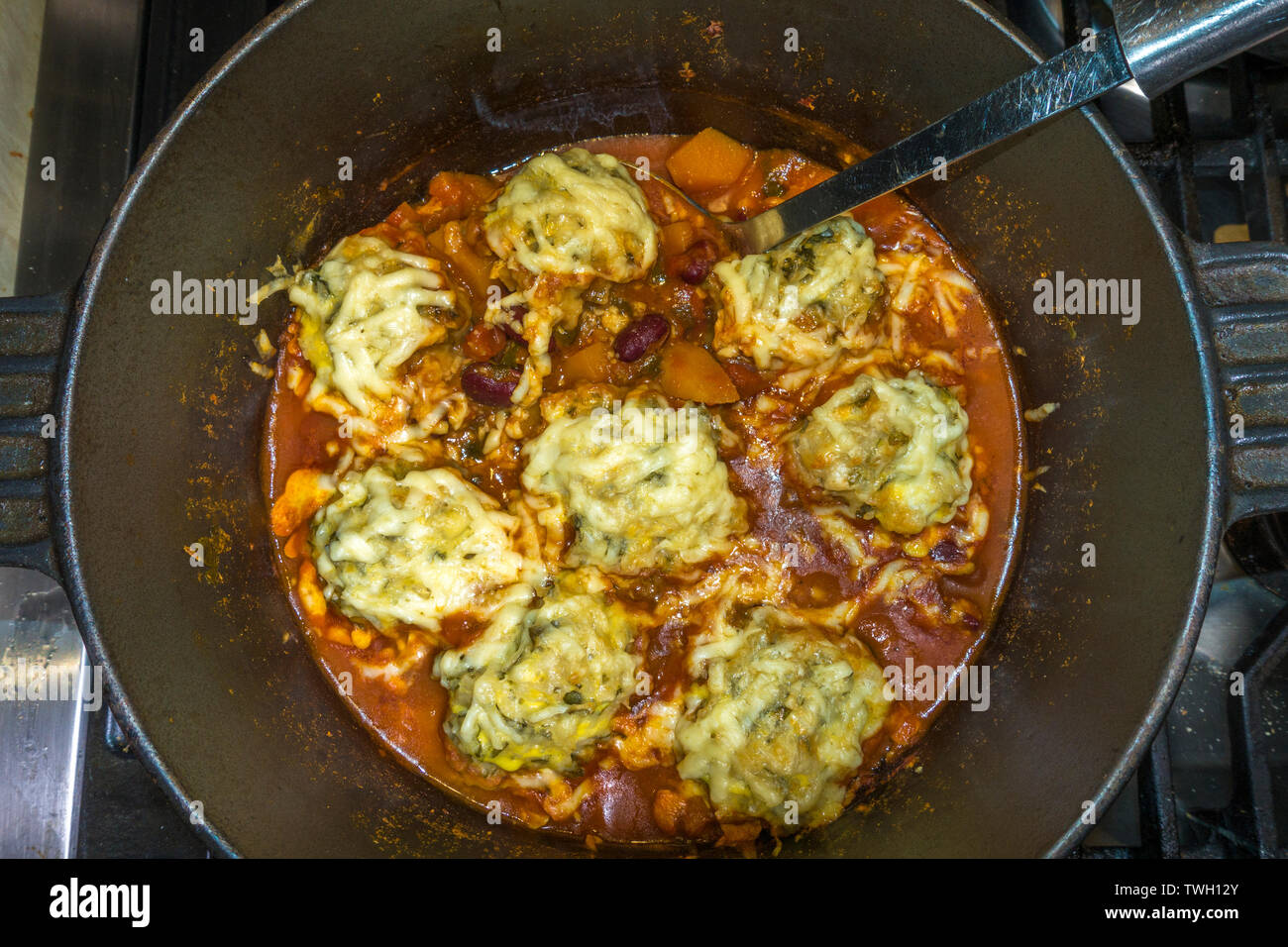 Indian stew cooking in a deep pan - cheese topped dumplings with spiced beans and vegetables. Stock Photo