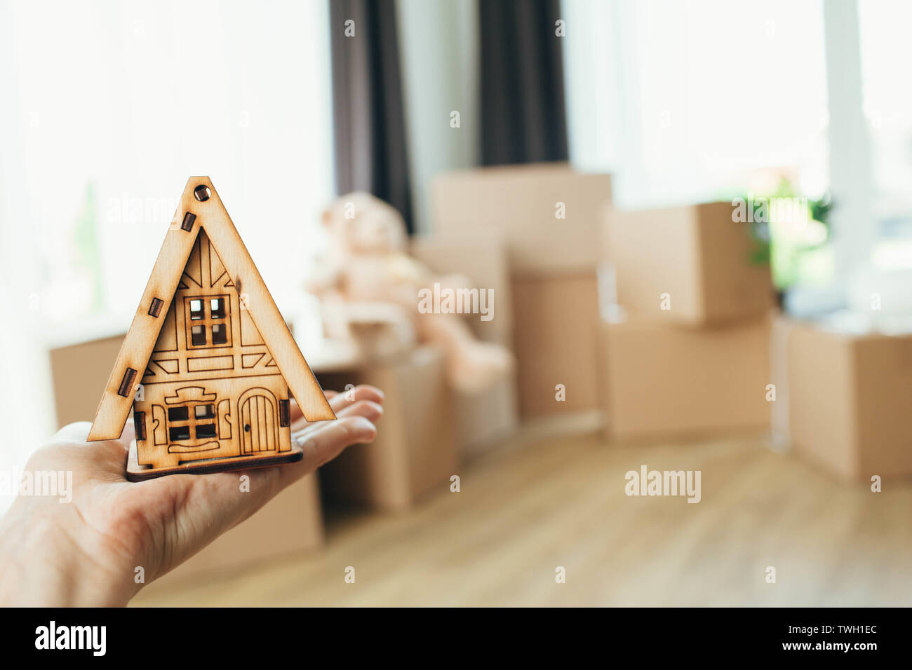 moving to a new home, buying a home. woman holding a miniature wooden small house on the background of cardboard boxes Stock Photo