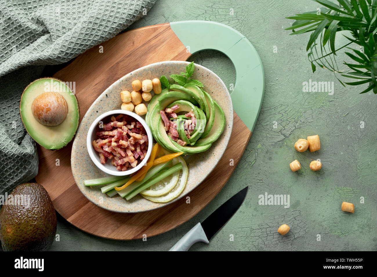Keto diet, top view of avocado rose salad with bacon cubes and smoked cheese seasoned with lemon, mint leaf and sea salt on green textured background Stock Photo