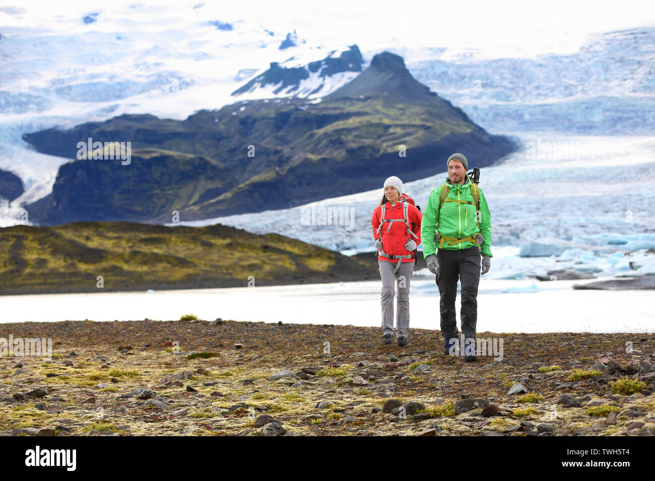 Adventure hiking travel couple trekking on Iceland. People by glacier and glacial lagoon / lake of Fjallsarlon, Vatna glacier, Vatnajokull National Park. Couple visiting Icelandic nature landscape. Stock Photo