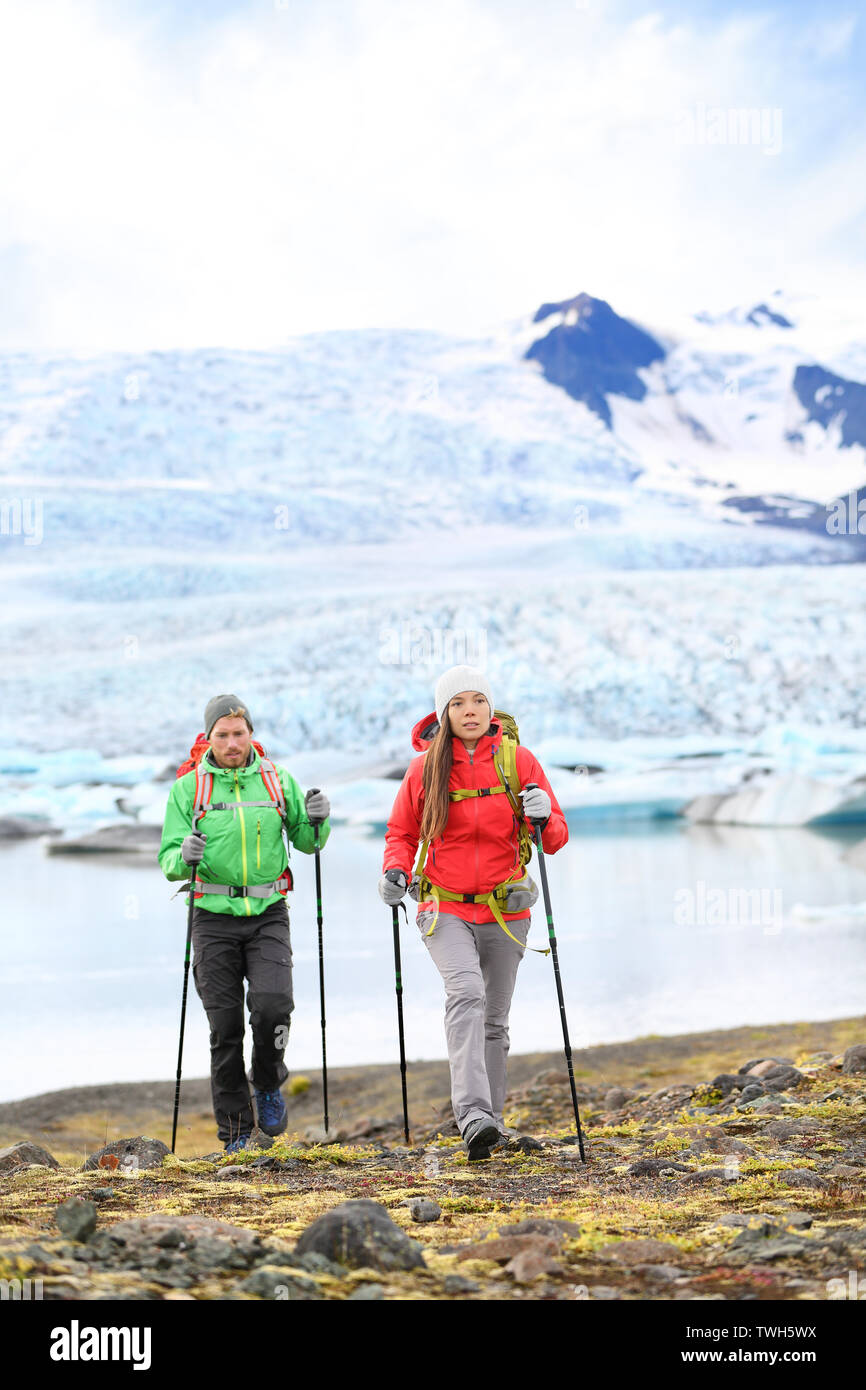 Adventure hikers travel people walking with hiking poles on Iceland by glacier and glacial lagoon / lake of Fjallsarlon, Vatna glacier, Vatnajokull National Park. Couple visiting Icelandic nature. Stock Photo