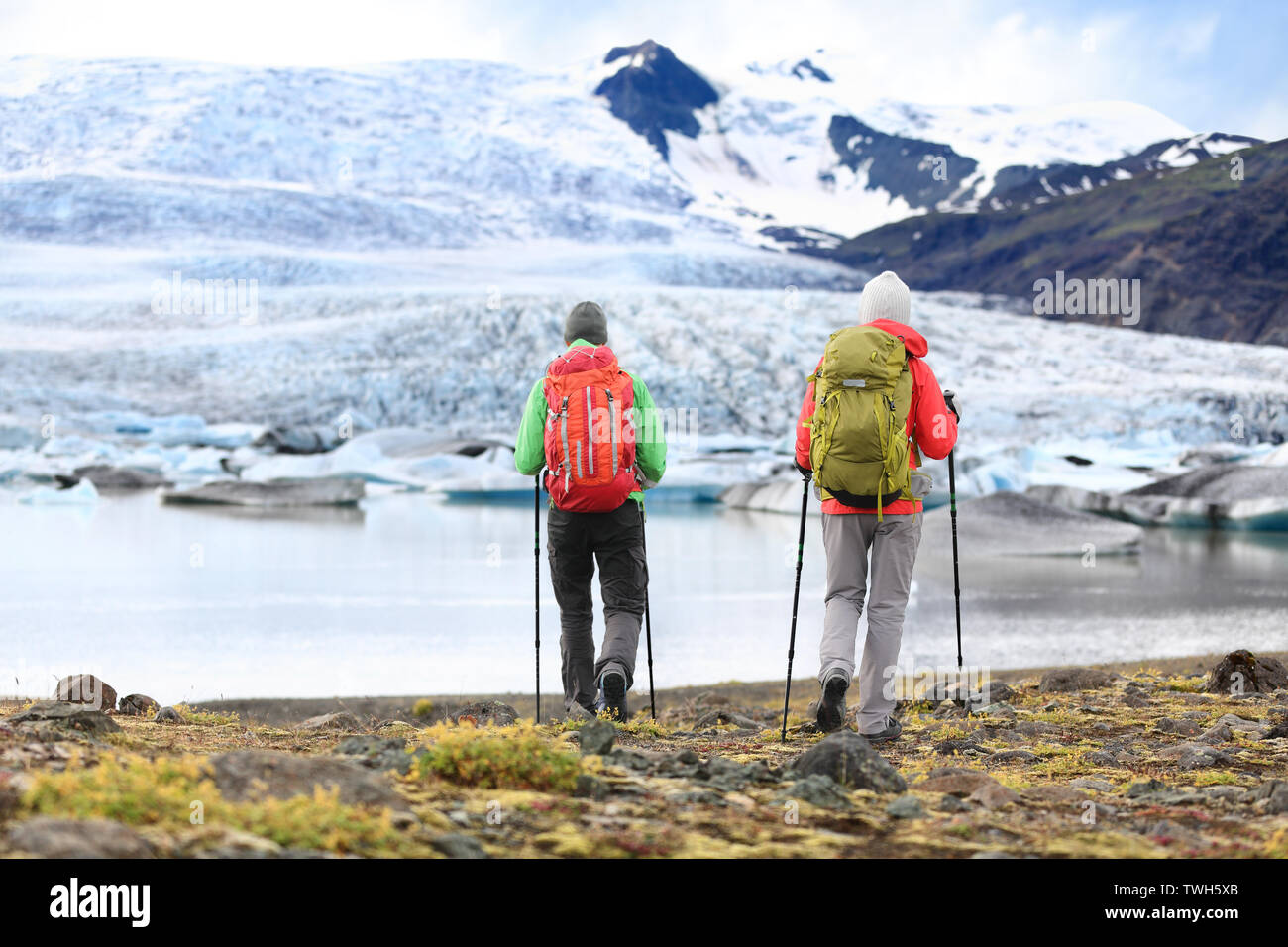 Hikers - people on adventure travel on Iceland. Hiking man man woman walking to glacier and glacial lagoon / lake of Fjallsarlon, Vatna glacier, Vatnajokull National Park. Couple in active lifestyle. Stock Photo