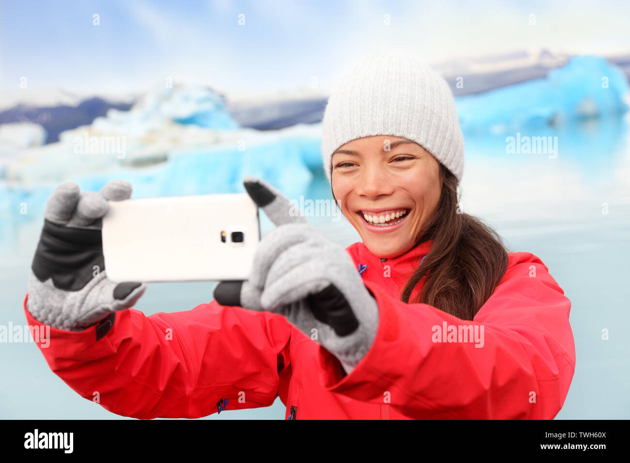 Woman taking selfie self portrait photo by Jokulsarlon glacial lagoon / glacier lake on Iceland. Happy tourist on travel using smartphone enjoying beautiful Icelandic nature landscape with Vatnajokull Stock Photo