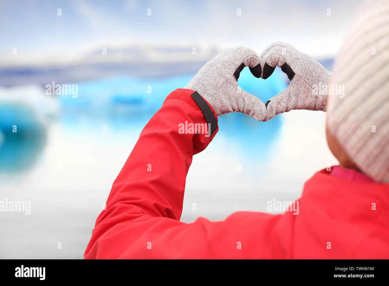 Love for Iceland - hand heart by Jokulsarlon. Woman showing hand heart sign with icebergs on glacial lagoon / glacier lake. Stock Photo