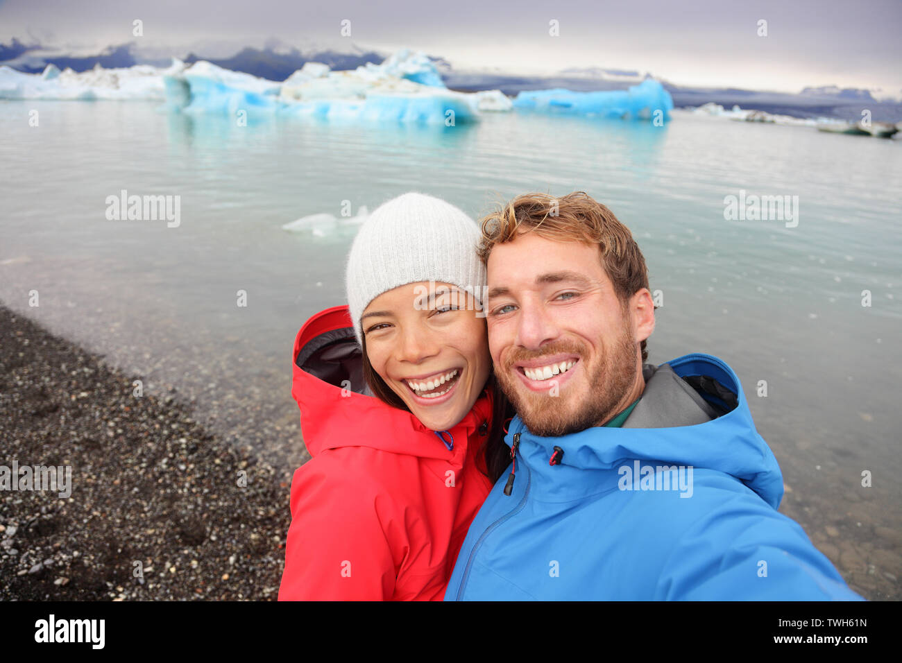 Couple taking selfie self portrait photo by Jokulsarlon glacial lagoon / glacier lake on Iceland. Happy tourists on travel enjoying beautiful Icelandic nature landscape with Vatnajokull in backround. Stock Photo