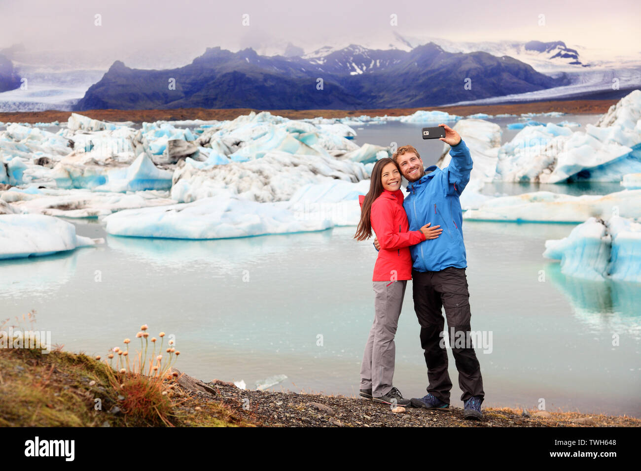 Iceland - couple taking selfie self portrait photo by Jokulsarlon glacial lagoon / glacier lake. Happy tourists on travel enjoying beautiful Icelandic nature landscape with Vatnajokull in backround. Stock Photo