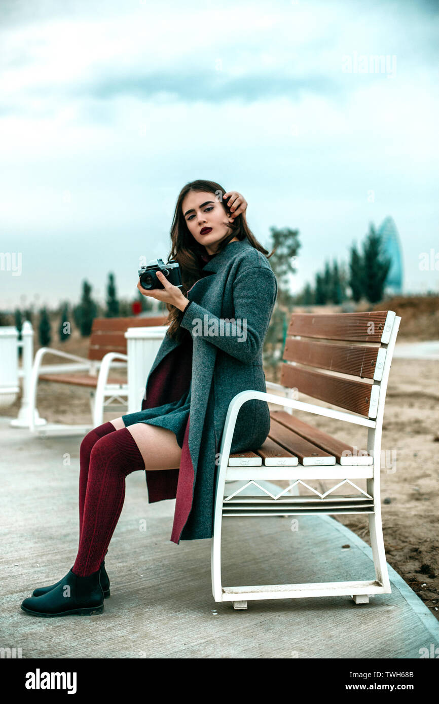 Young Beautiful Girl In Burgundy Stockings And Gray Coat Sitting