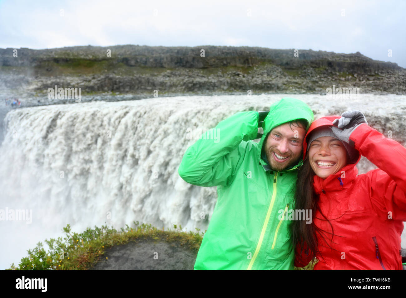 Travel couple fun in raincoats by Dettifoss waterfall on Iceland. People visiting famous tourist attractions and landmarks on Diamond Circle. Stock Photo