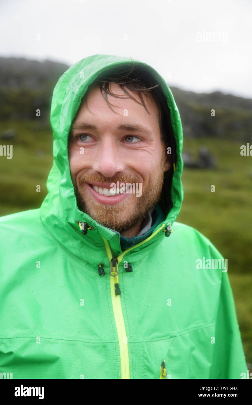 Rain jacket - man smiling outdoors on rainy day. Portrait of male model wearing green rain jackets outside living outdoor lifestyle. Stock Photo