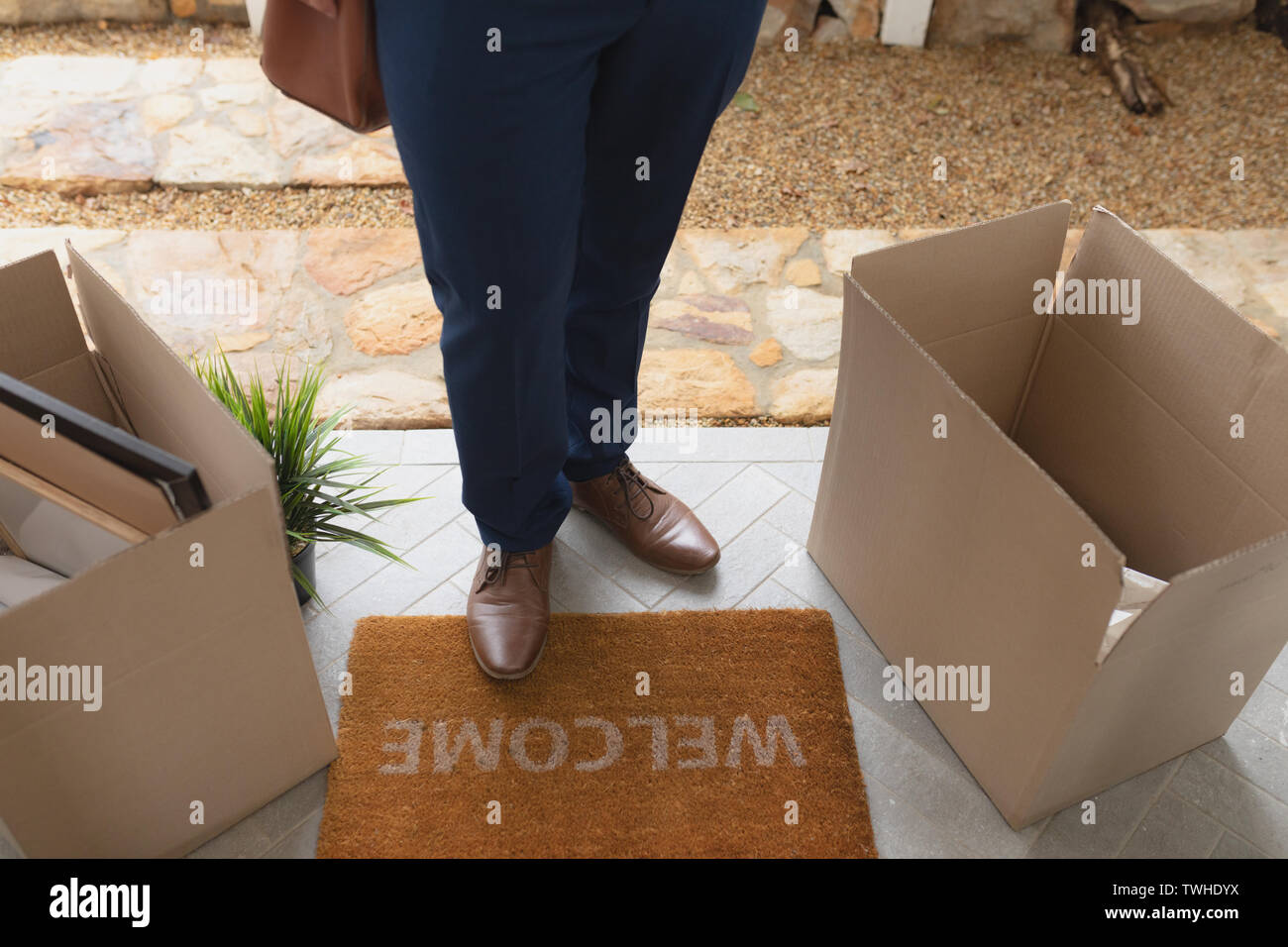 Man with cardboard boxes standing on welcome mat in front of door at ...