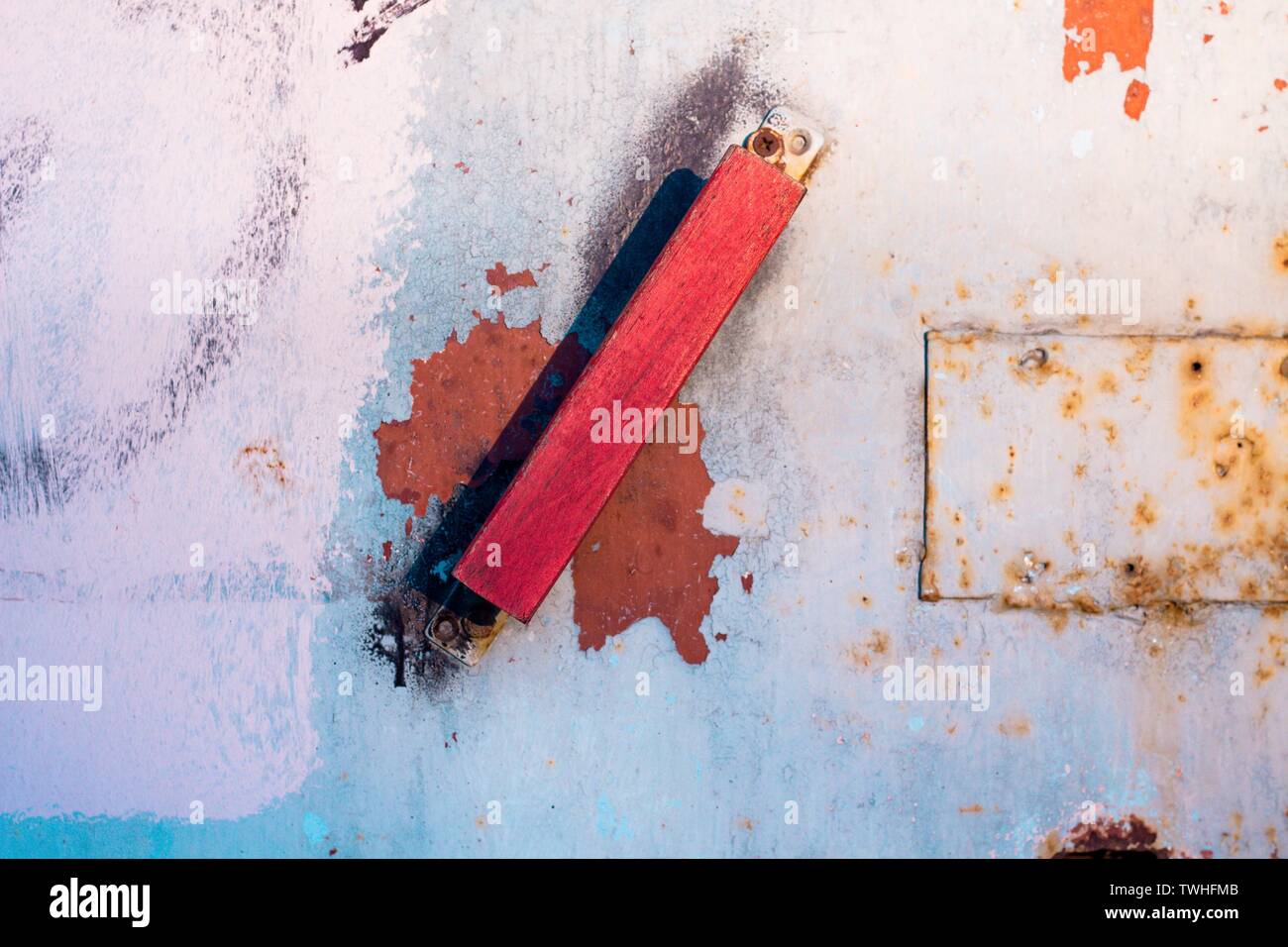 Wooden door handle red shade. The handle is attached to a metal door which is covered with rust and old paint. Stock Photo