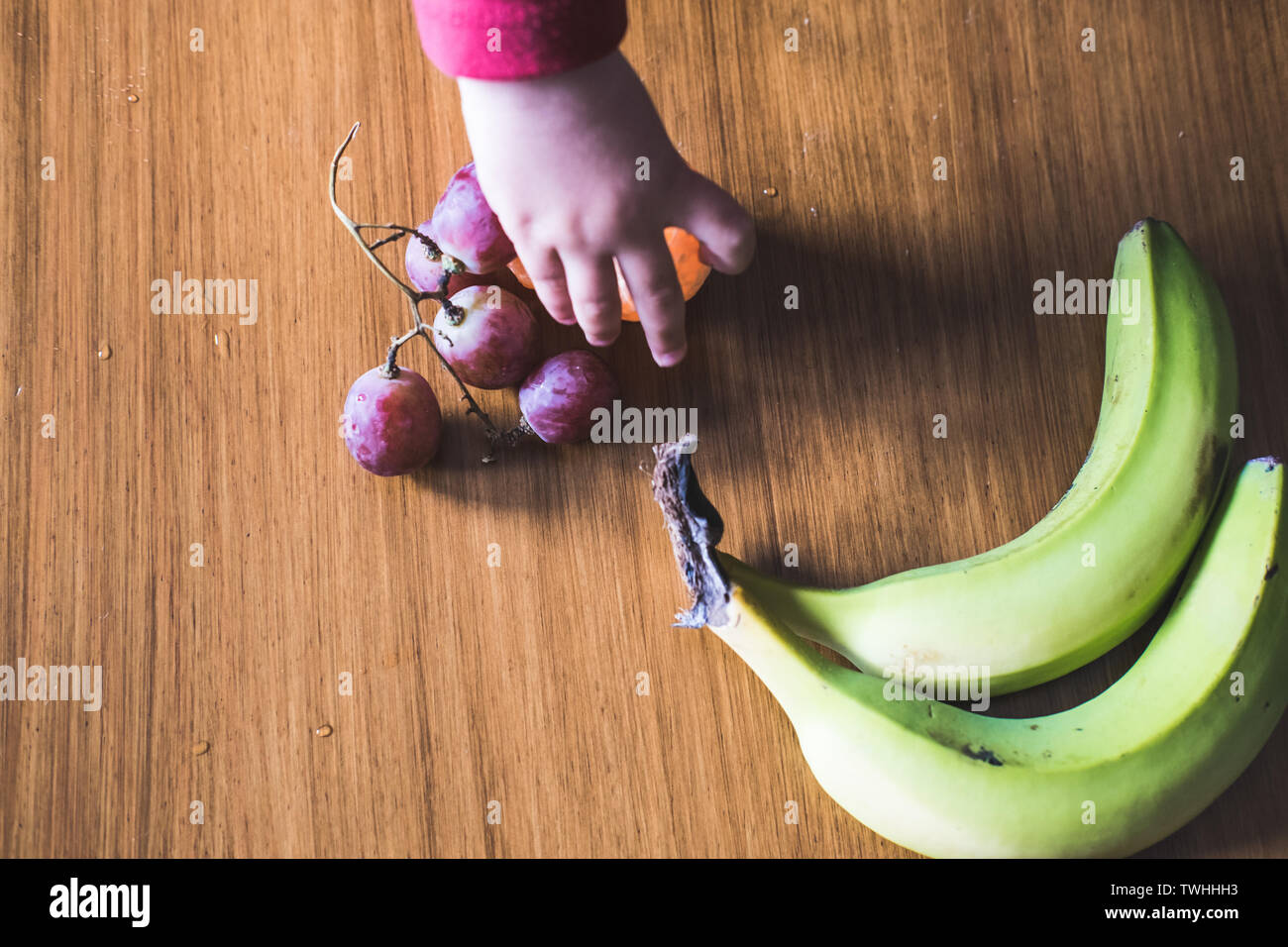 Baby s hand manipulating different fruits on a wooden table Stock Photo