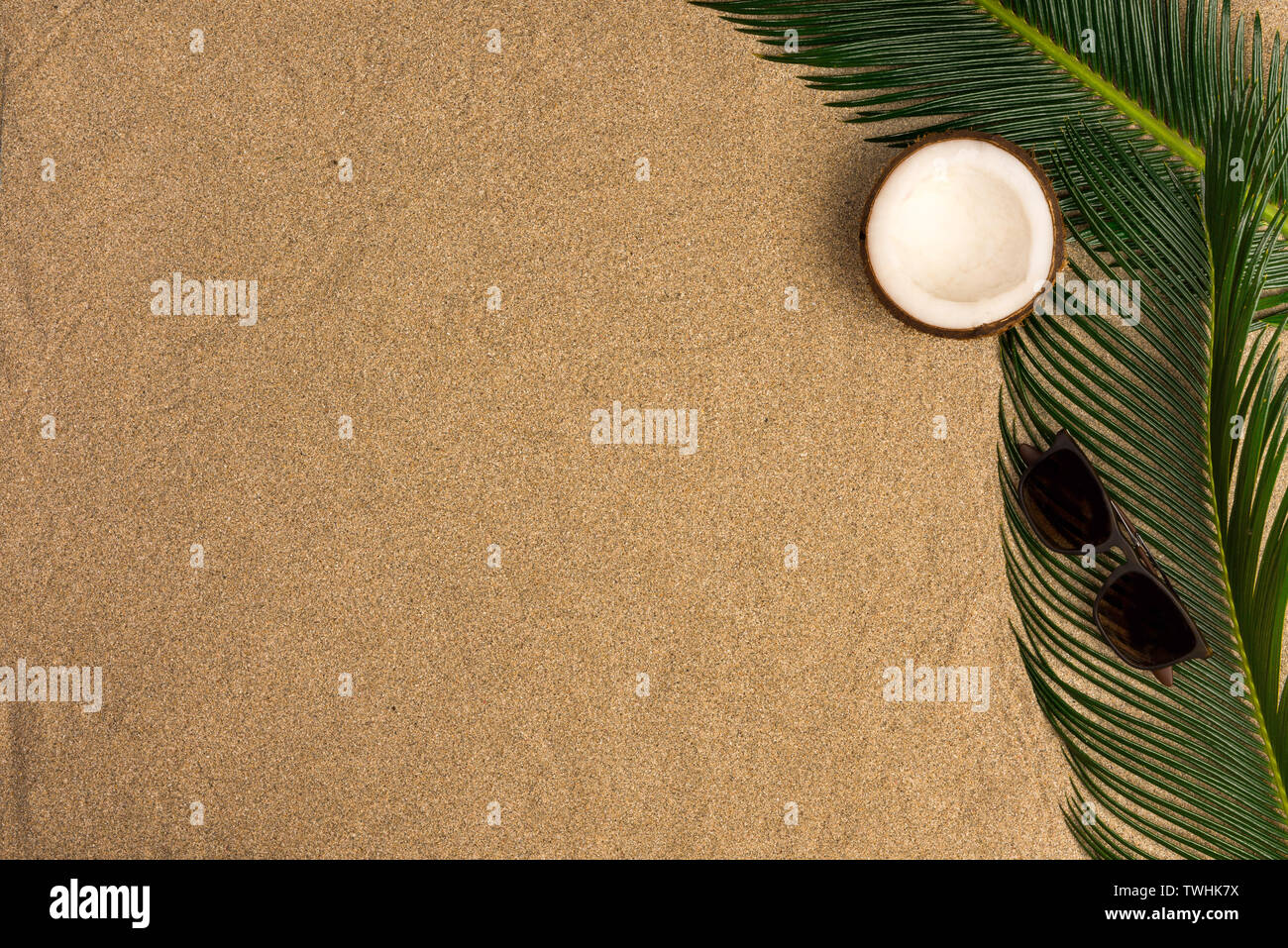 Beach theme on the sand background. Palm leaves, coconut, sunglasses on the sand. Top view. Stock Photo