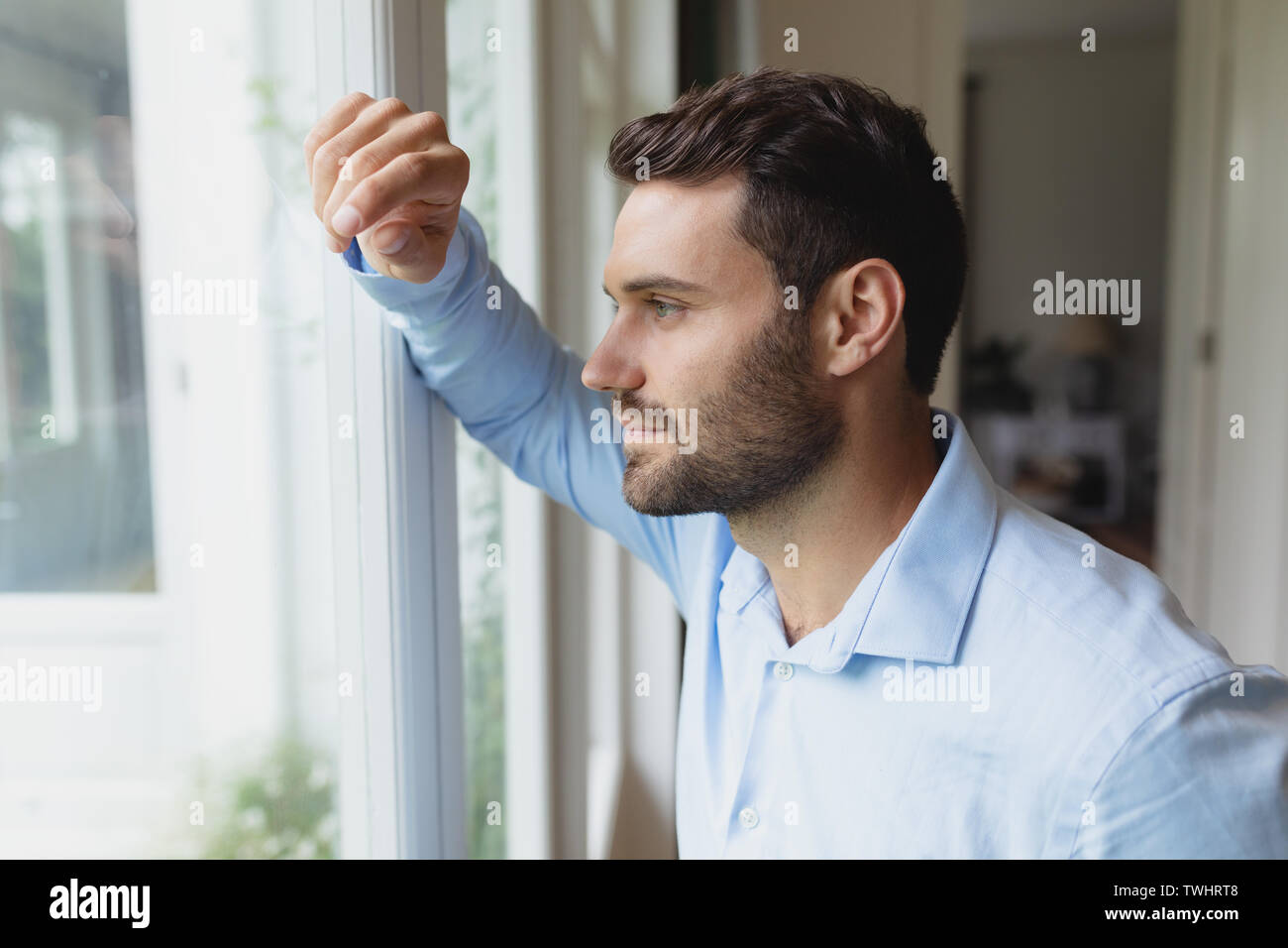 Thoughtful man looking outside through window in a comfortable home Stock Photo