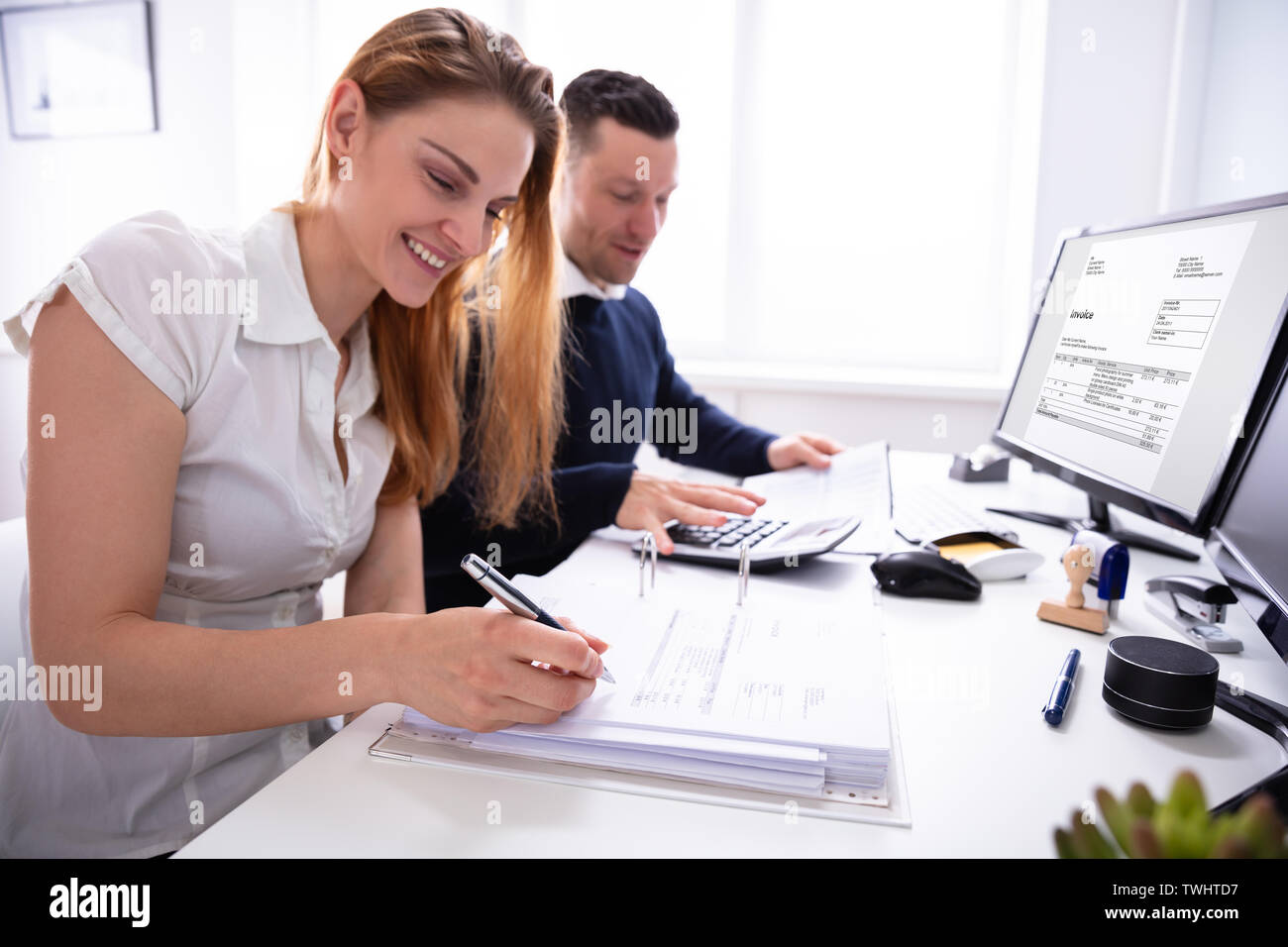 Side View Of Two Businesspeople Calculating Invoice With Calculator On Desk At Workplace Stock Photo