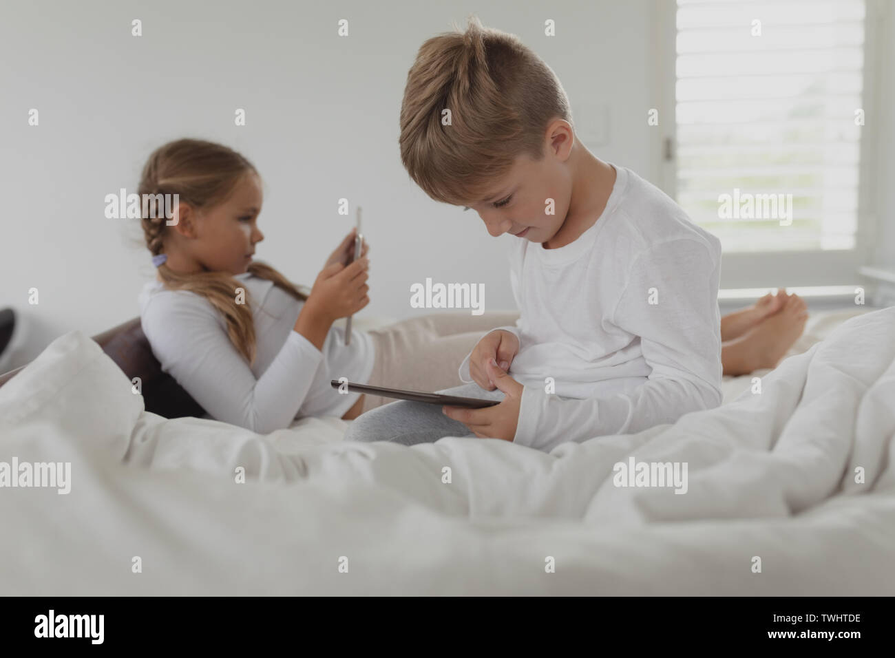 Siblings using digital tablet on bed in bedroom at comfortable home Stock Photo