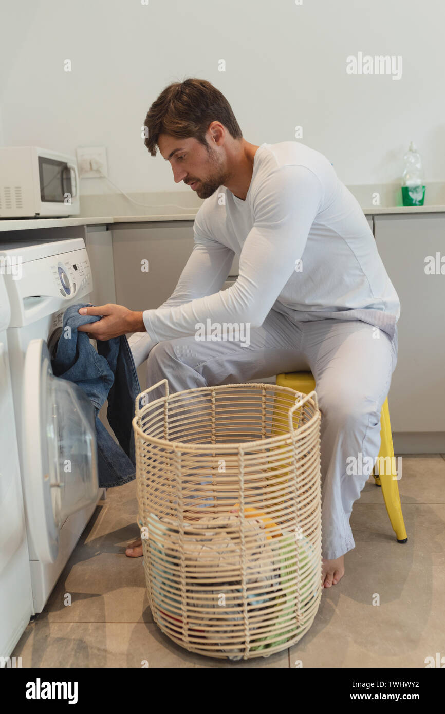 Man putting clothes in the washing machine, in the kitchen, worried because  he has to wash a lot of clothes. Close up Stock Photo - Alamy