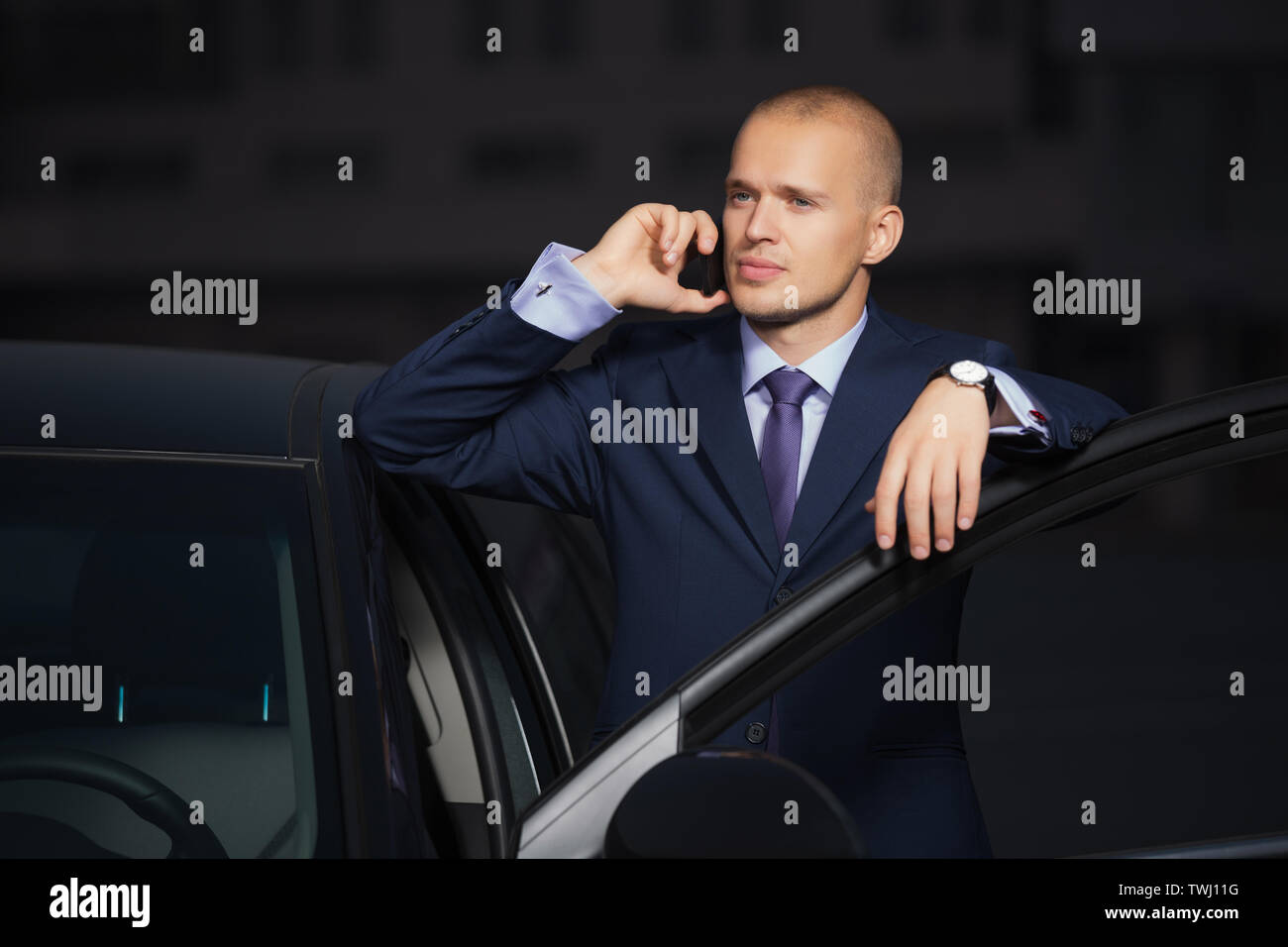 Young businessman calling on cell phone leaning on his car  Stylish trendy male model wearing dark blue business suit Stock Photo