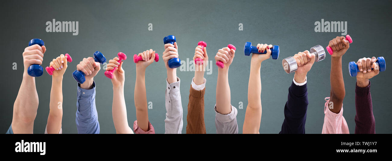 Group Of Man And Woman's Hand Holding Dumbbells In A Row Against Green Background Stock Photo