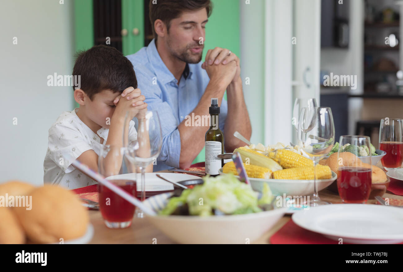 Father and son praying before having lunch at dining table Stock Photo