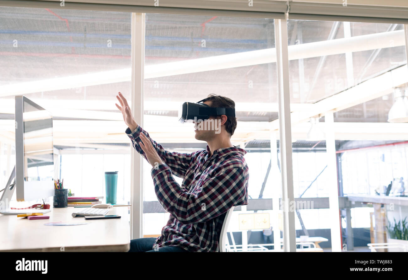 Male graphic designer using virtual reality headset at desk Stock Photo