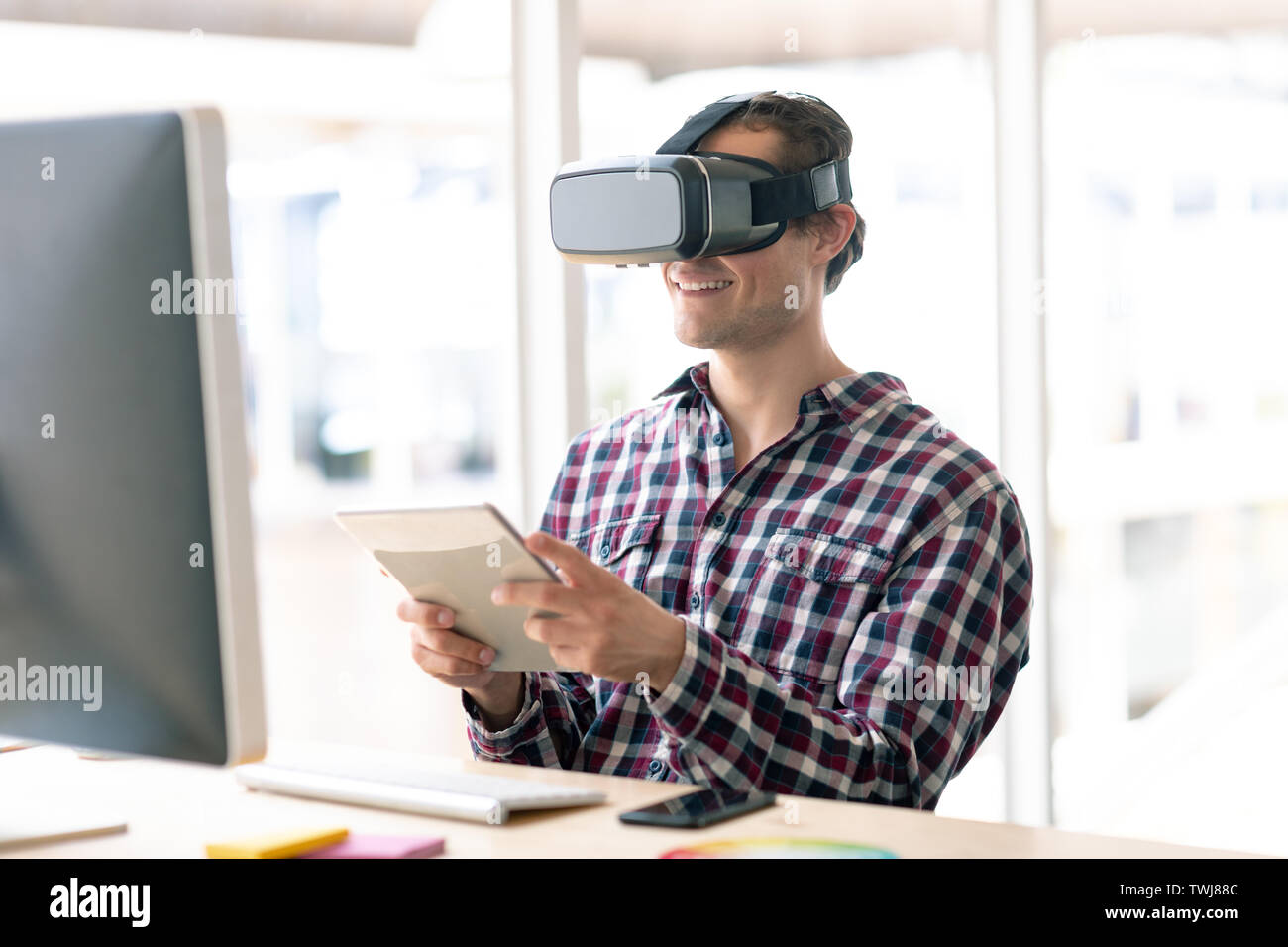 Male graphic designer using virtual reality headset while working on digital tablet at desk Stock Photo