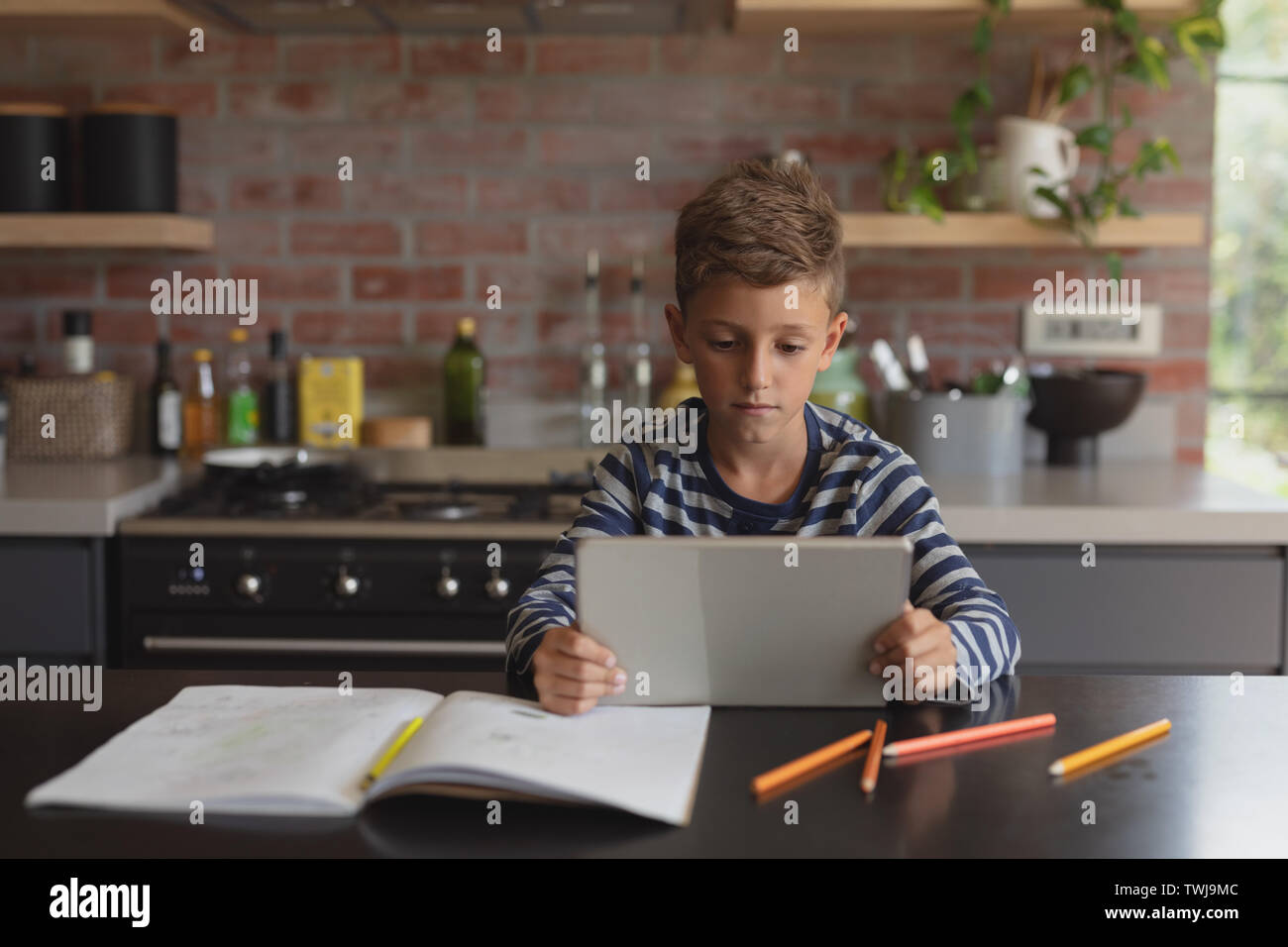 Boy using digital tablet at table in kitchen at home Stock Photo