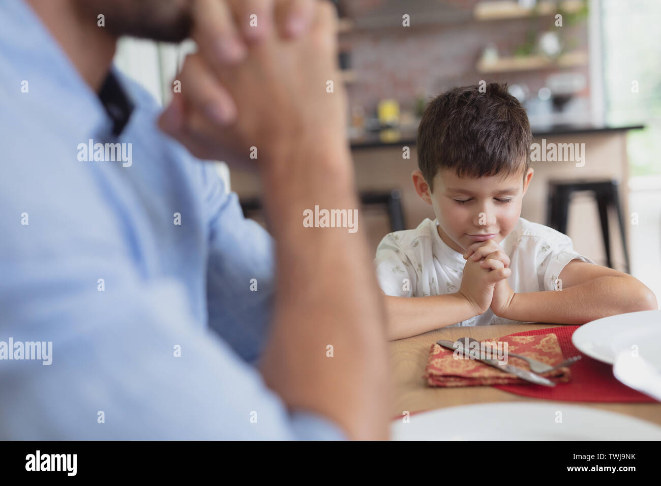 Father and son praying before having lunch at dining table Stock Photo