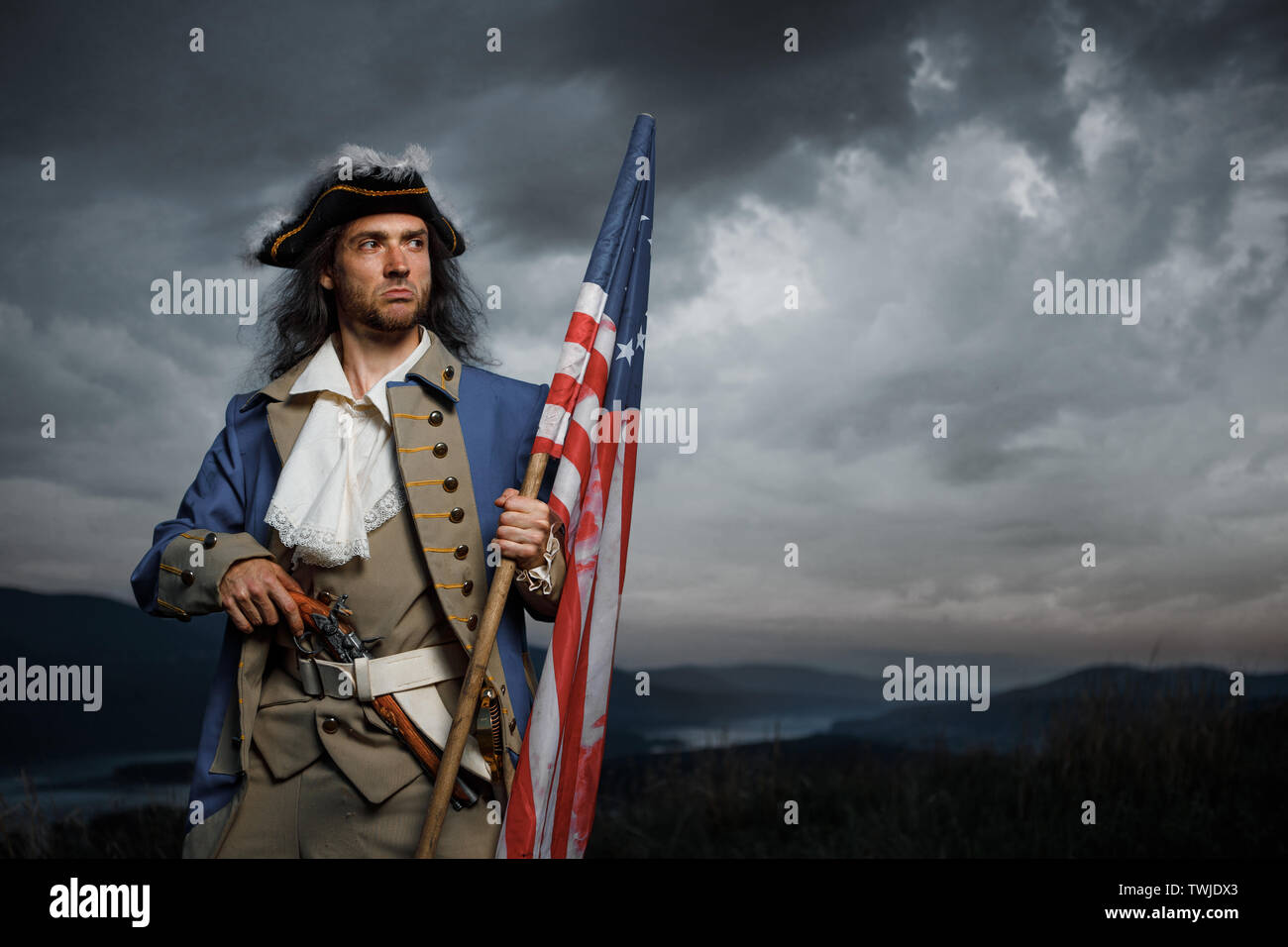 Soldier of United States War of Independence with flag and pistol posing over dramatic sky. 4th july History Concept photo Stock Photo