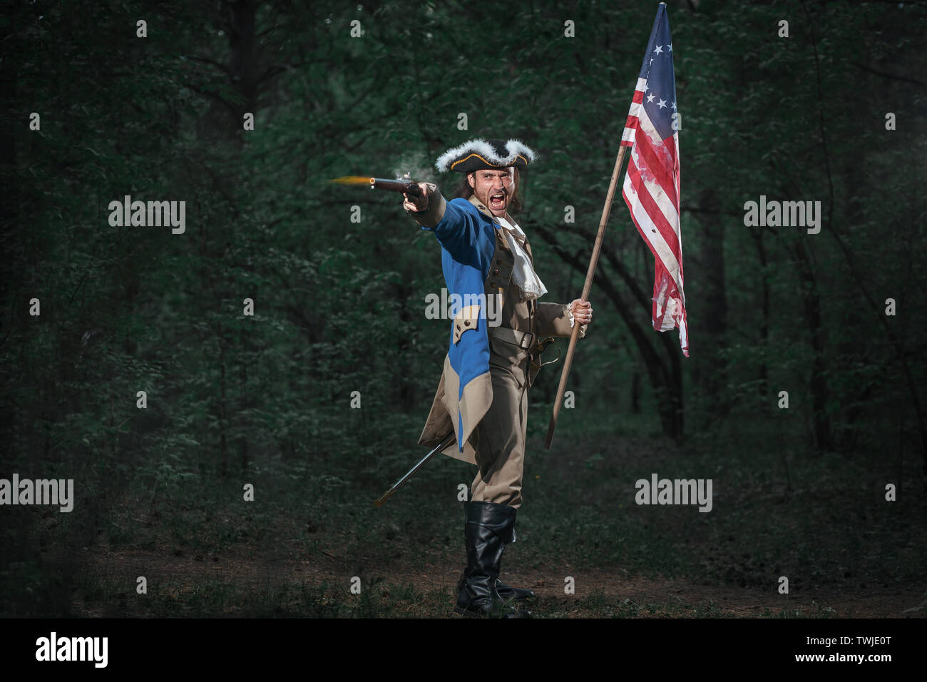 Epic Portrait of man dressed as soldier of american revolution war of United States aims from pistol with flag. 4 july independence day of USA concept Stock Photo