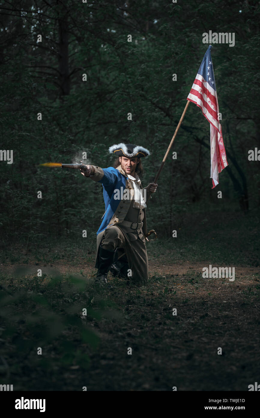 Epic Portrait of man dressed as soldier of american revolution war of United States aims from pistol with flag. 4 july independence day of USA concept Stock Photo