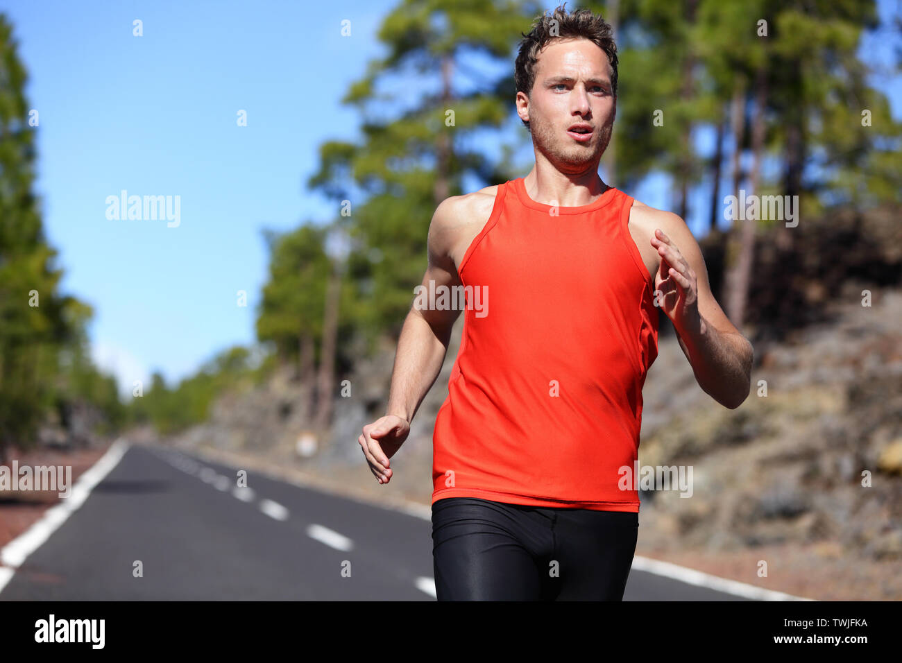 Sprinting runner man running at fast speed. Male sport sprinter training hard. Young strong male fitness model during run outdoors in beautiful landscape. Stock Photo