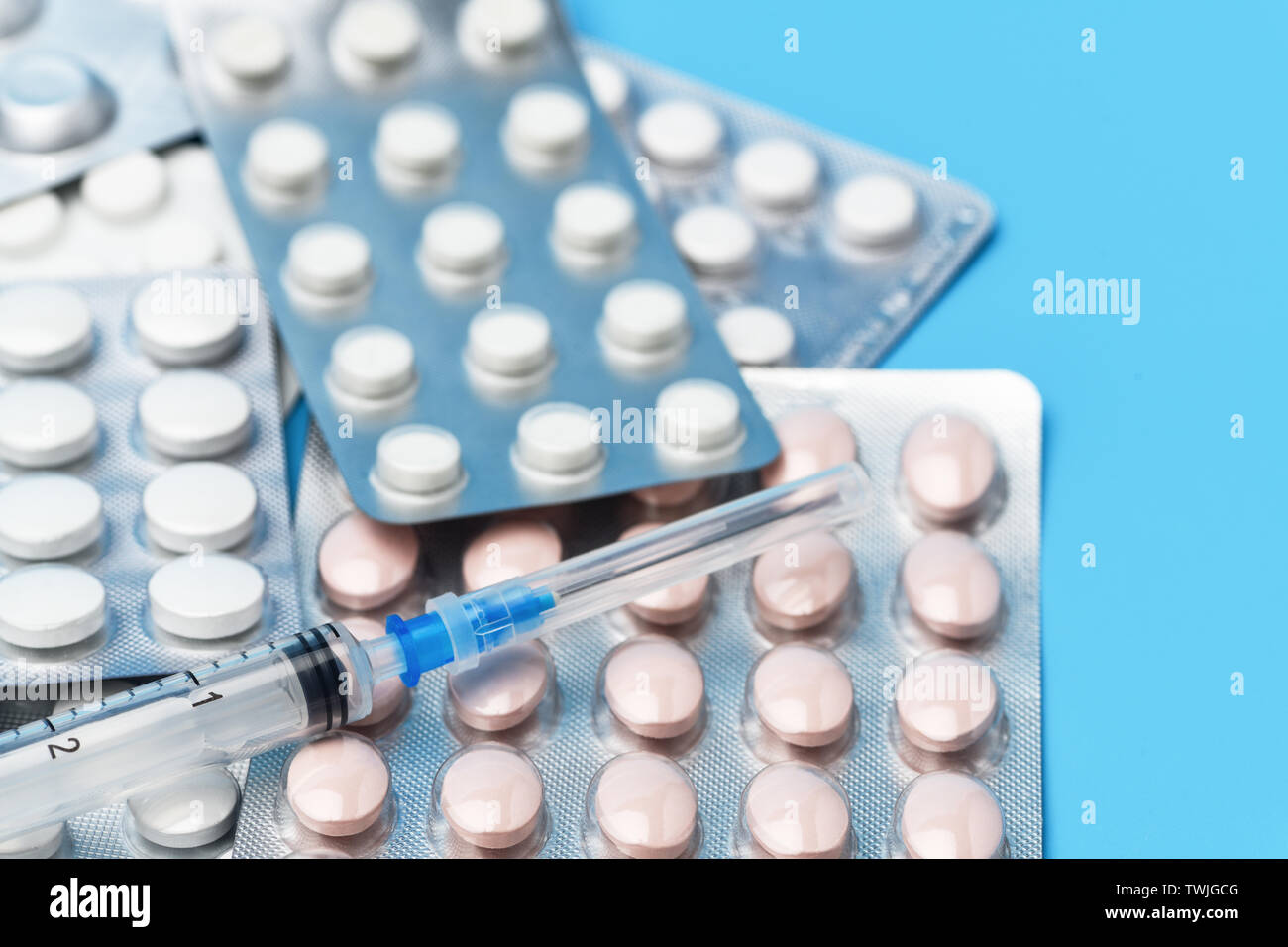 A lot of pills of different color and lies on top of the syringe with needle. Pills close up. Medical background Stock Photo