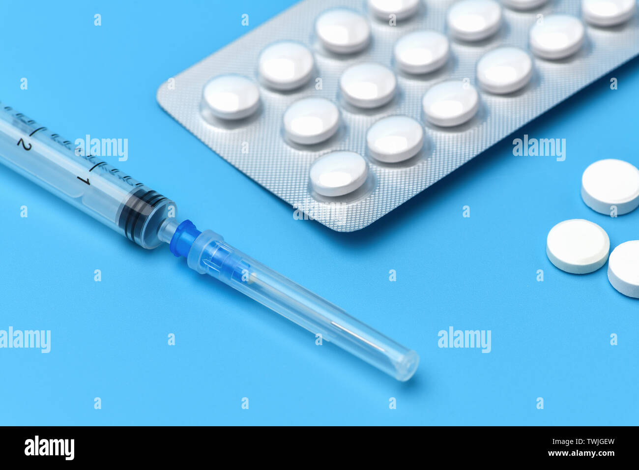 Many tablets are on a blue background, at the bottom is a syringe with an injection. Drugs and pills prescription background. Pharmaceutical preparati Stock Photo