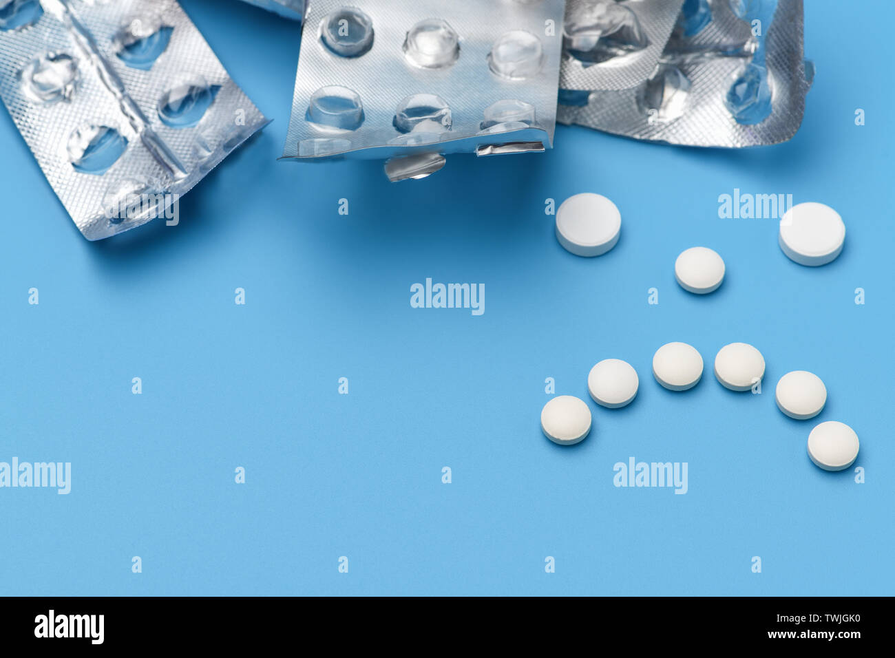 Sad face with white pills. A lot of empty packages of pills on a blue background, lined with a sad grimace of pills Stock Photo