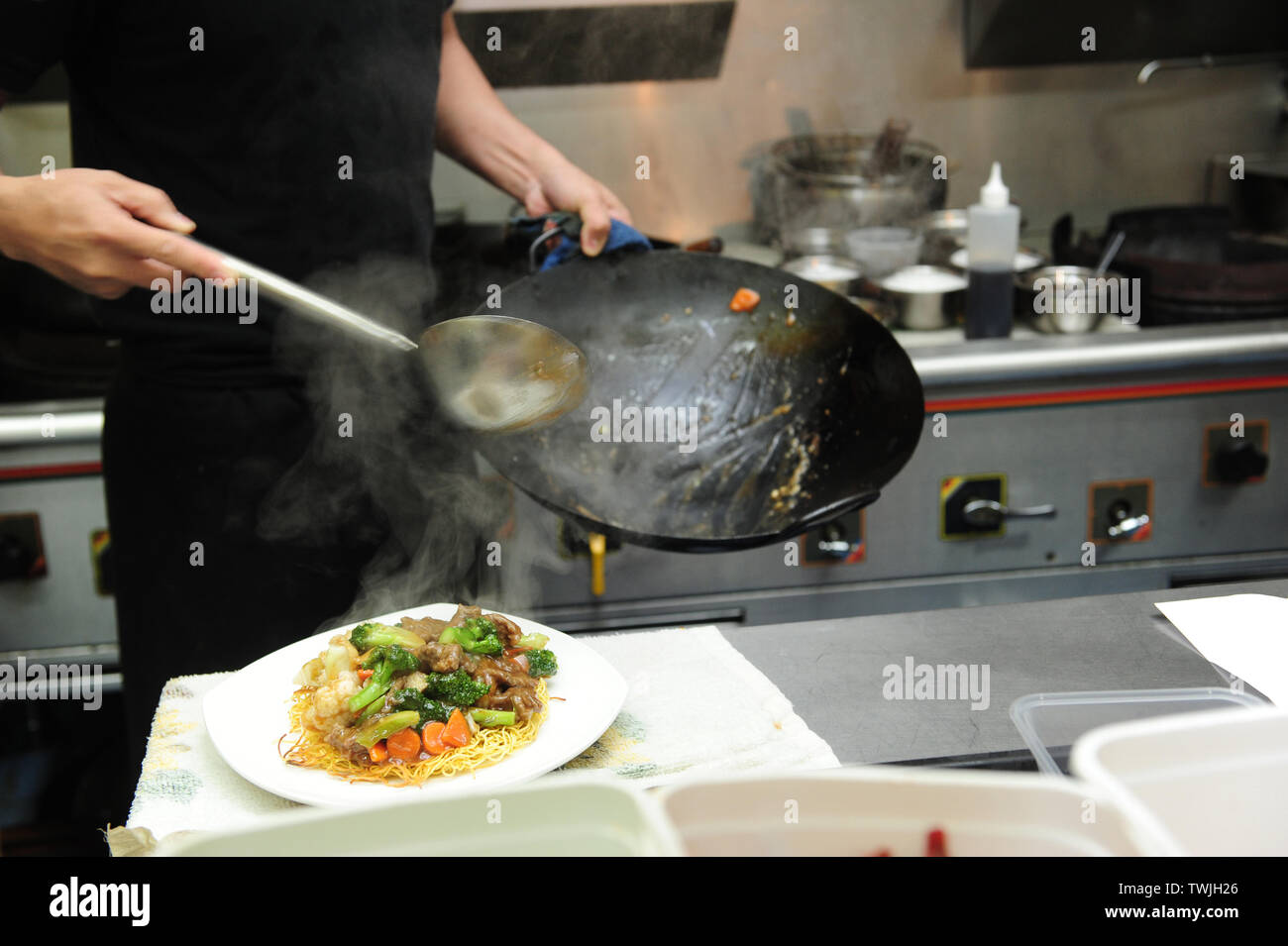 Close up of chef plating the noodle on to a plate from a wok, chinese takeaway, asian food, kitchen. Stock Photo
