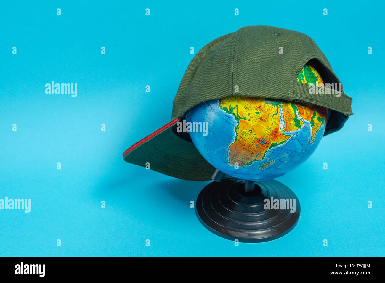 Globe with a green baseball cap on it on a blue background. Stock Photo