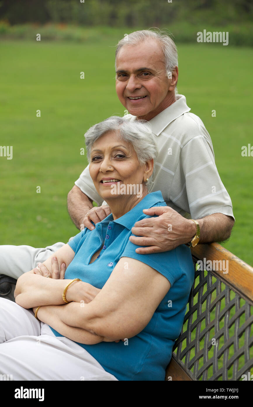 Old Couple Sitting On A Park Bench And Smiling Stock Photo