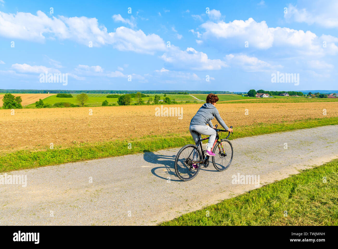 Young woman riding bicycle on rural road in spring landscape of Burgerland near Strem village, Austria Stock Photo