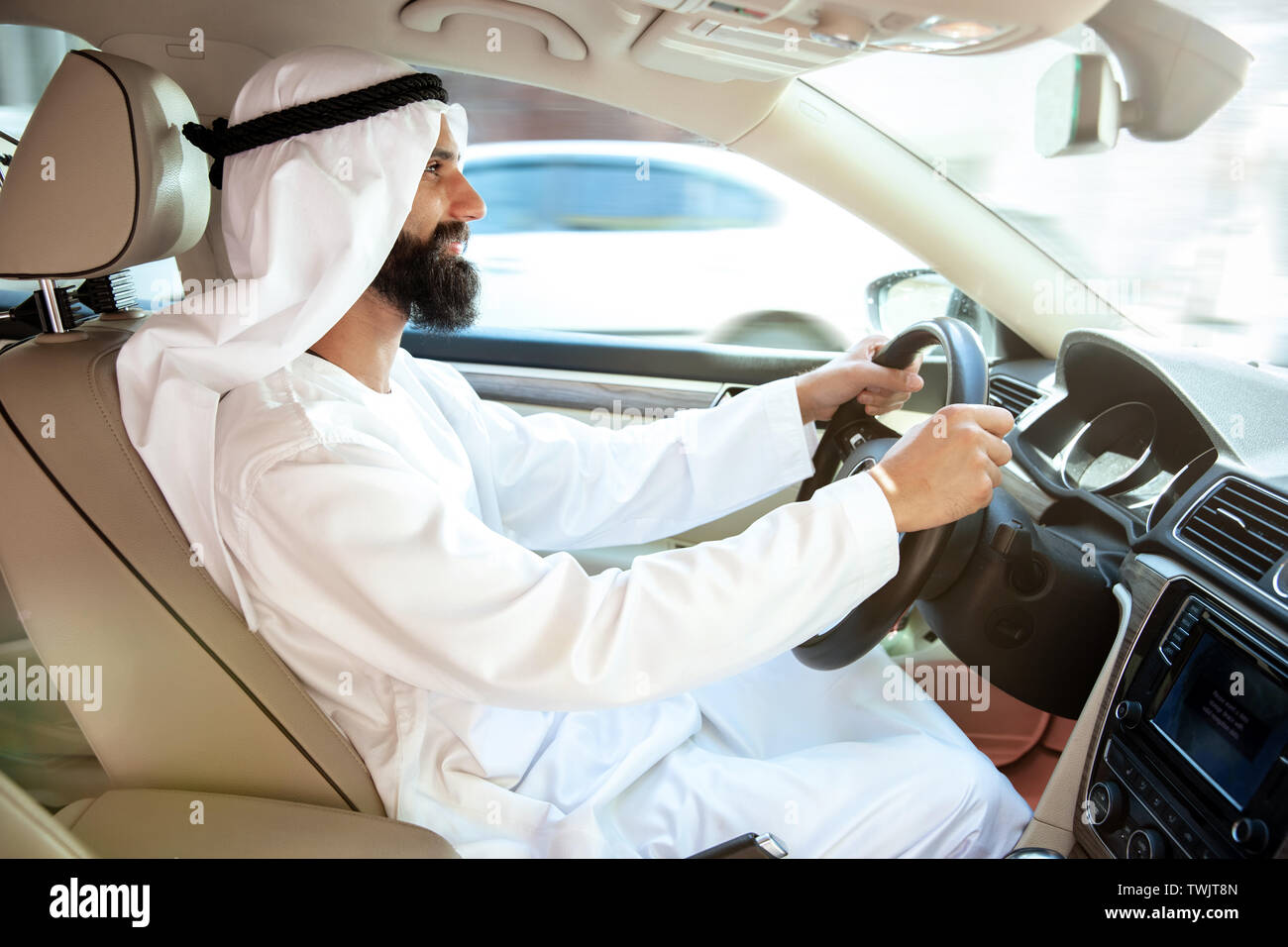 Successful arab saudi businessman riding his car or driving full of emotions at sunny day. Male model as an enterpreneur. Concept of business, finance, modern technologies, start up, economy. Stock Photo