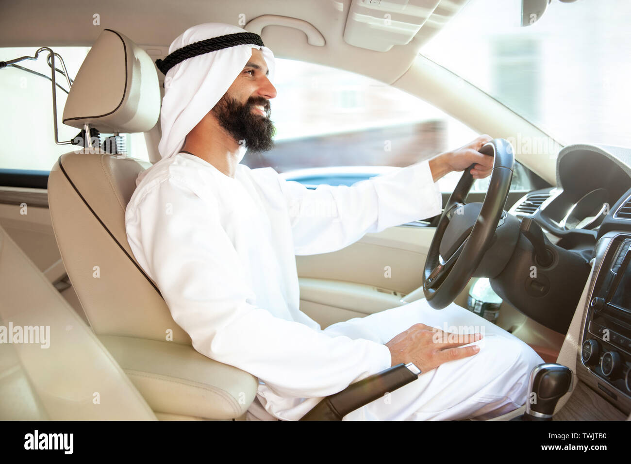 Successful arab saudi businessman riding his car or driving full of emotions at sunny day. Male model as an enterpreneur. Concept of business, finance, modern technologies, start up, economy. Stock Photo