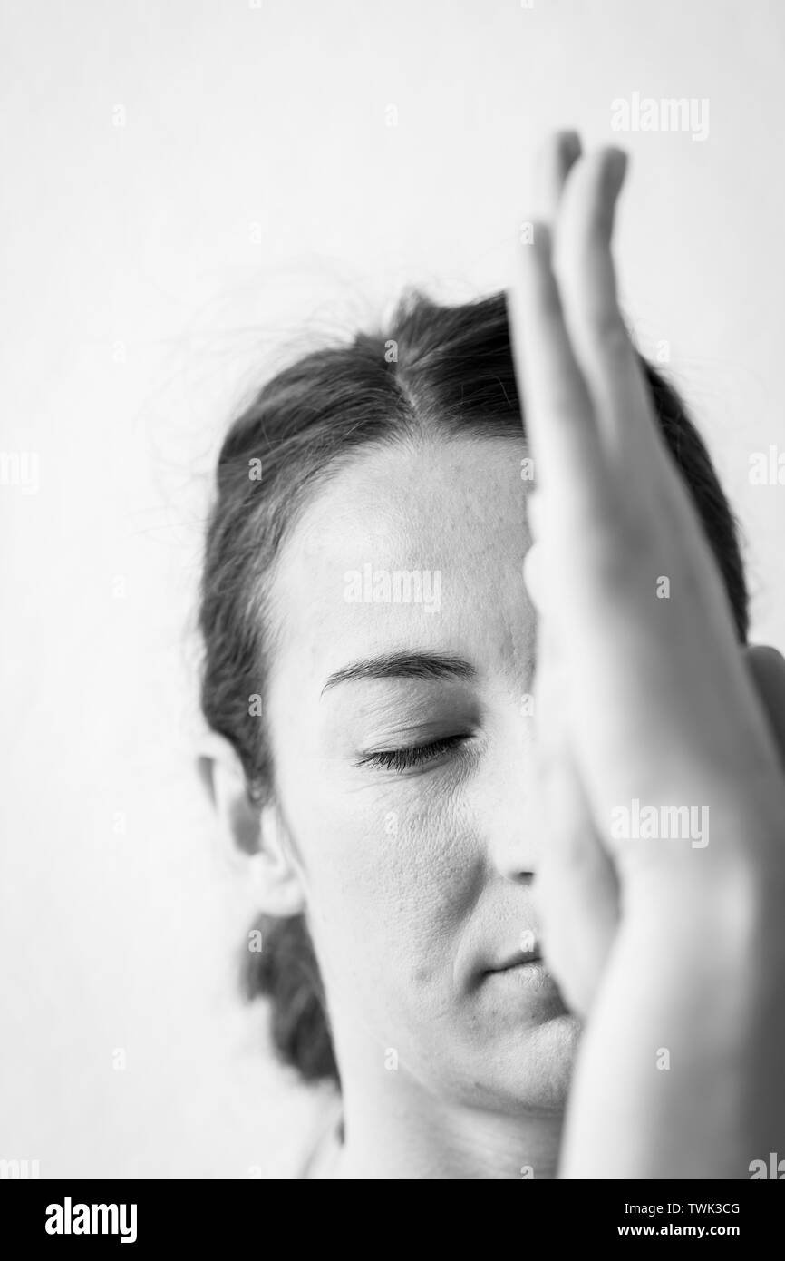 Vertical closeup, black and white front view of a brunette woman in her 30s concentrated with closed eyes doing eagle arms yoga pose or Garudasana. Stock Photo