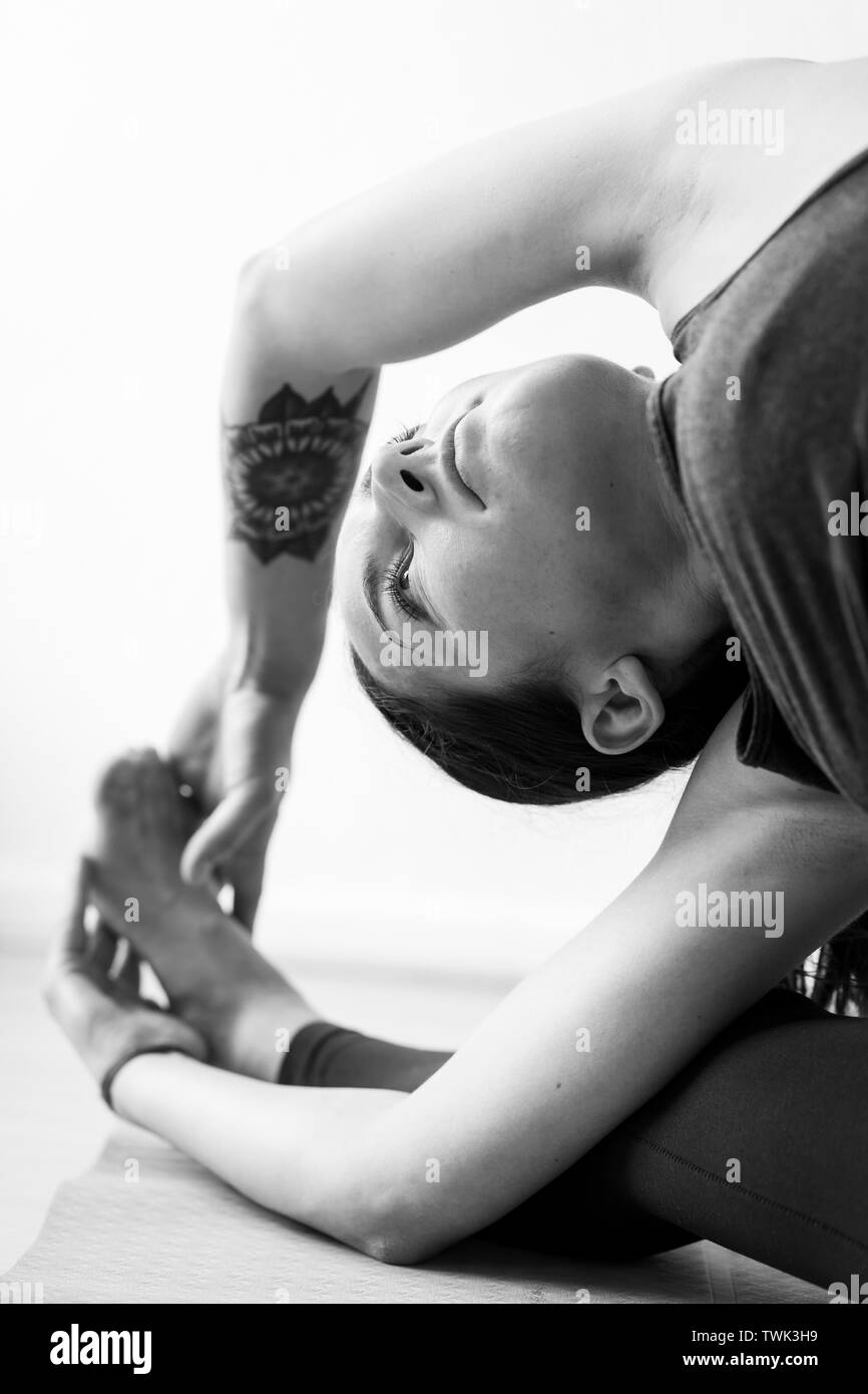 A brunette woman in her 30’s practicing yoga at home. One woman concentrated on a revolved Head-of-Knee Pose or Parivrtta Janu Sirsasana, vertical vie Stock Photo