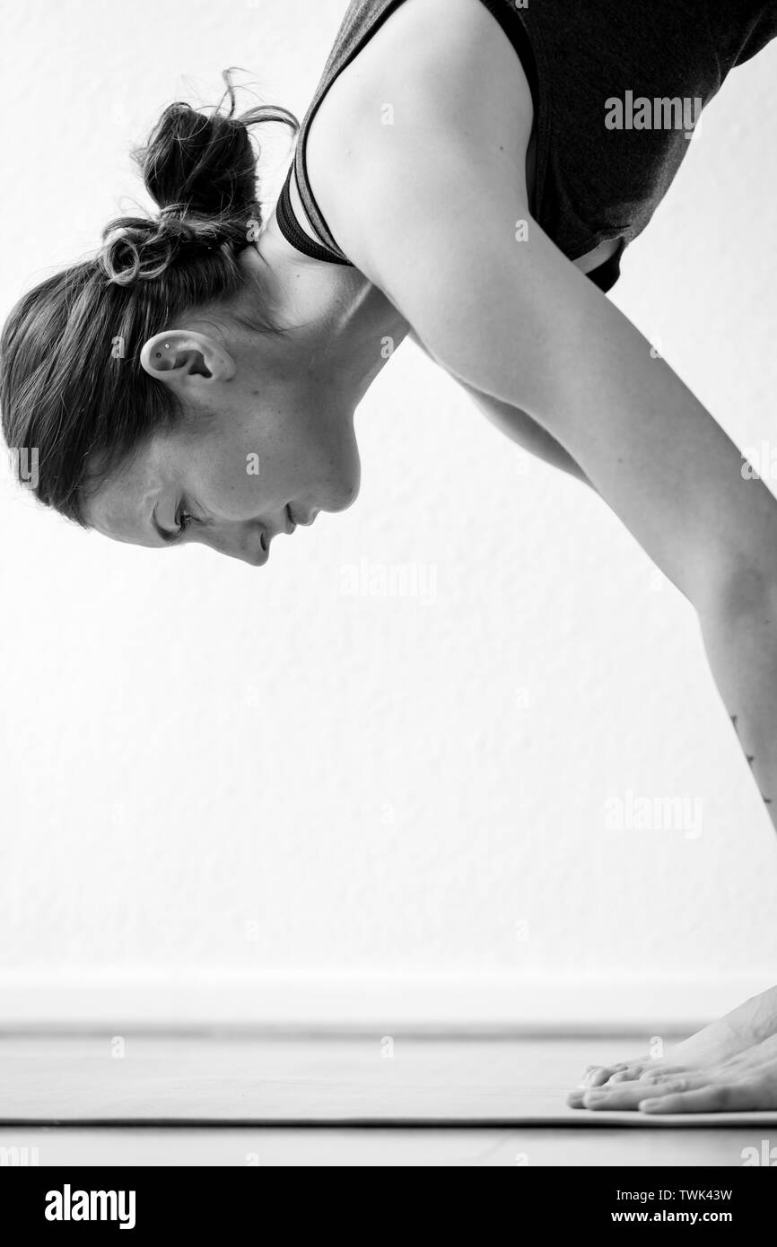 Close-up side view of a young woman in her earl y30's on a standing forward bending asana or yoga pose Stock Photo