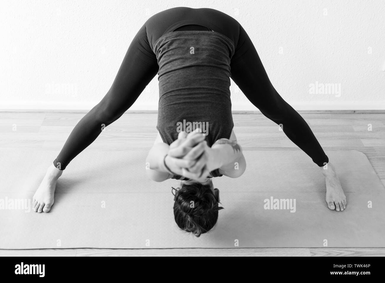 An unrecognizable brunette woman in her 30’s practicing yoga at home. One woman concentrated on a aide-legged forward bend asana, or yoga posture. Stock Photo