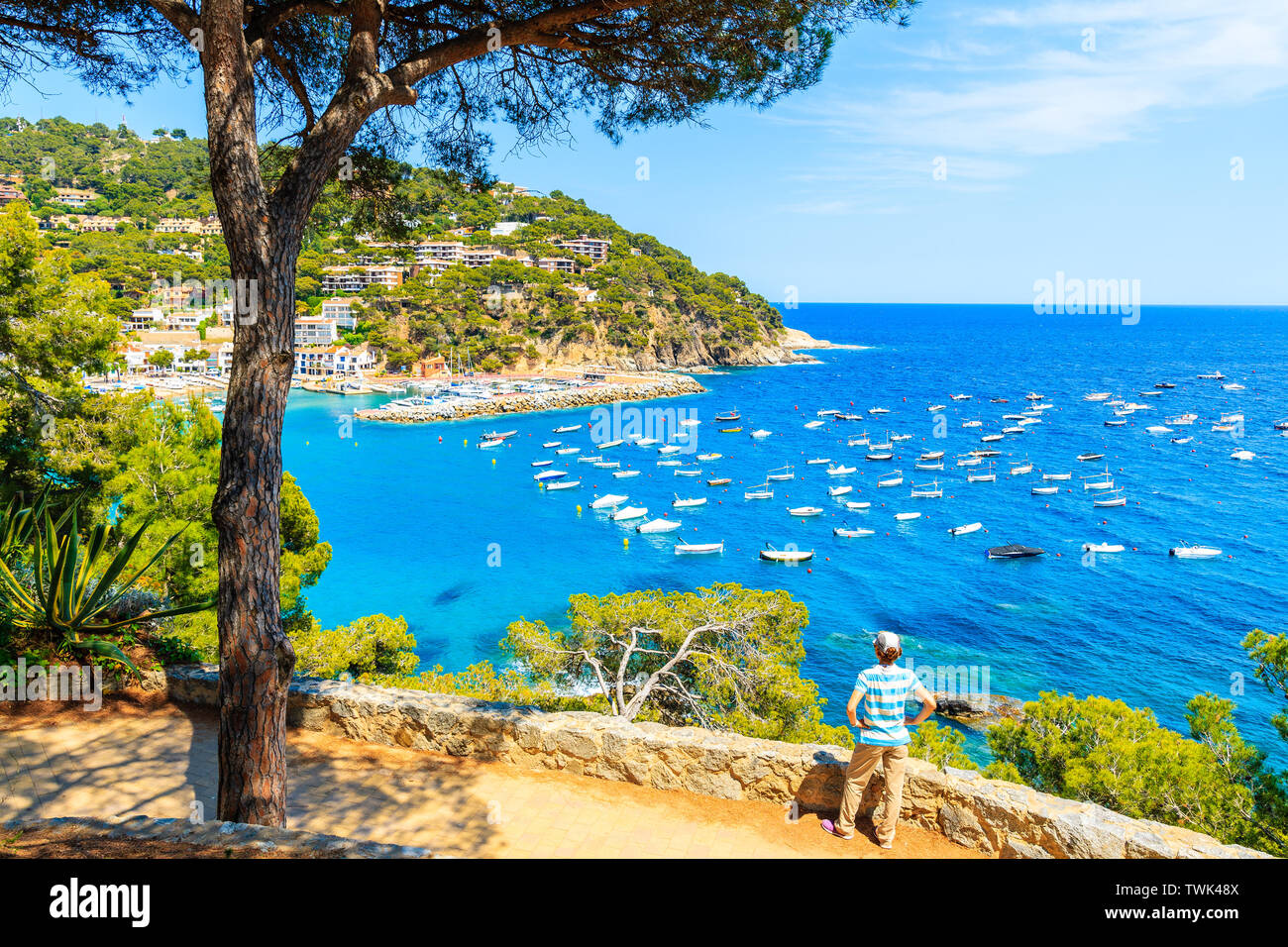 Young woman tourist standing on viewpoint over beautiful bay with boats on sea near Llafranc village, Costa Brava, Spain Stock Photo