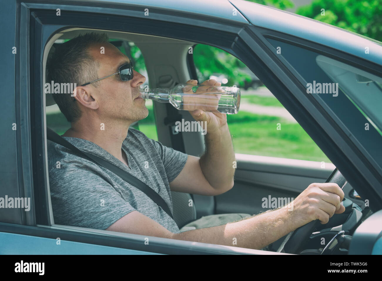 Man driving a car with a bottle of alcohol drink in hand. Don't drink ...