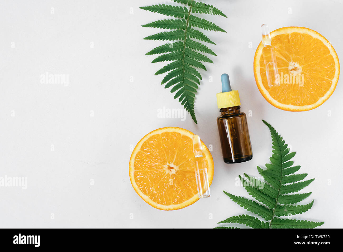 Natural cosmetic skincare serum packaging with leaf fern and fresh juicy  orange fruit on white background. Beauty vitamin ingredient. alternative  medicine. Flat lay, top view, copy space Stock Photo