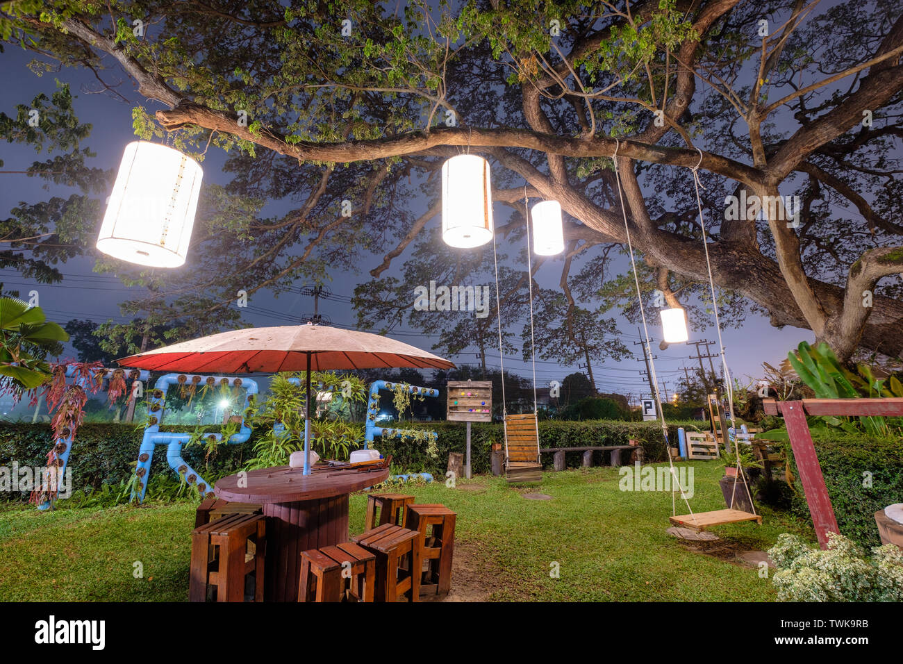 Big Rain tree decorative lighting craft lamp with wooden table chair on lawn in restaurant at dusk Stock Photo