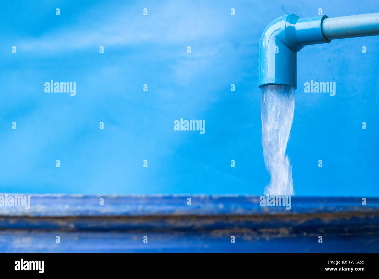 Blue pvc pipe with flowing water in bucket from groundwater Stock Photo